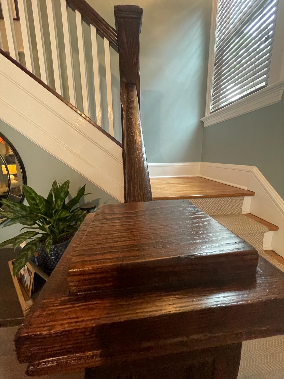 Richly stained oak handrail and newel post beside crisp white balusters